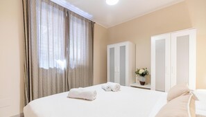 A hotel room with a large bed, a wardrobe, a nightstand with a vase, and a window with curtains. - THE VIEW by Design Studio (Bellano)
