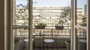 An open balcony with a table and chairs, potted plants, and a view of a building with multiple windows. - Milano Charming apartment, a unique home: central area, 2BDR, 2BTH, 4 Guests (Milano)