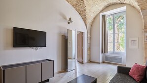 A modern living room with a flat-screen TV, a sofa, a coffee table, and a large arched window.
