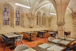A dining area with tables and chairs, stone arches, and large windows. - Bel Appartement spacieux lumineux, près du centre (Dijon)