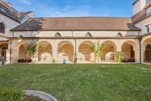 A courtyard with a central lawn, surrounded by arched walkways and buildings with stone walls and windows. - Bel Appartement spacieux lumineux, près du centre (Dijon)