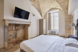 A bedroom with a stone fireplace, a flat-screen TV mounted on the wall, and a large bed. - Bel Appartement spacieux lumineux, près du centre (Dijon)