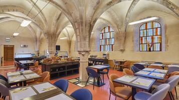A spacious room with high arched ceilings, multiple tables with chairs, and large windows with stained glass.