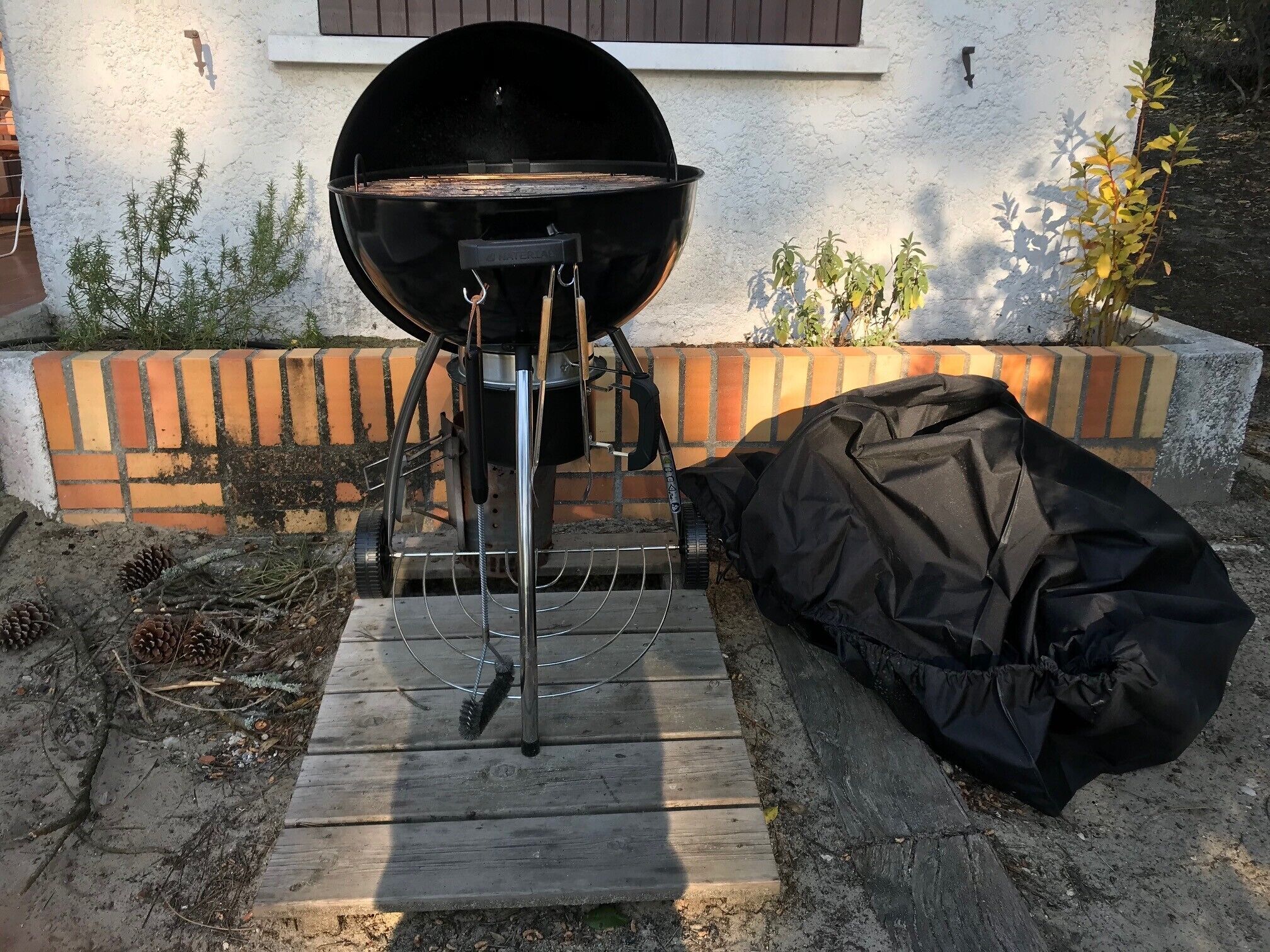 Una parrilla para barbacoa con iniciador de chimenea y una funda negra sobre una terraza de madera.
