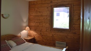 Ein Schlafzimmer mit Holzwandverkleidung, einem Bett mit Kissen, einem Nachttisch mit Lampe und einem Fenster mit Blick ins Freie.