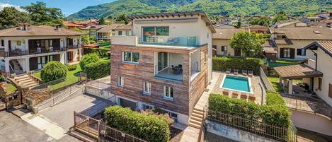 Una casa moderna de dos pisos con balcón, piscina y montañas al fondo.