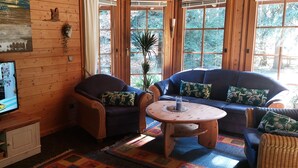 Een knus ingerichte kamer met houten wanden, een televisie, een bank, twee fauteuils en een klein houten tafeltje.