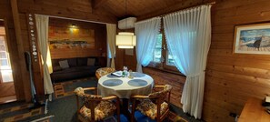 A cozy cabin interior with a round table, chairs, a sofa, and a painting on the wall.