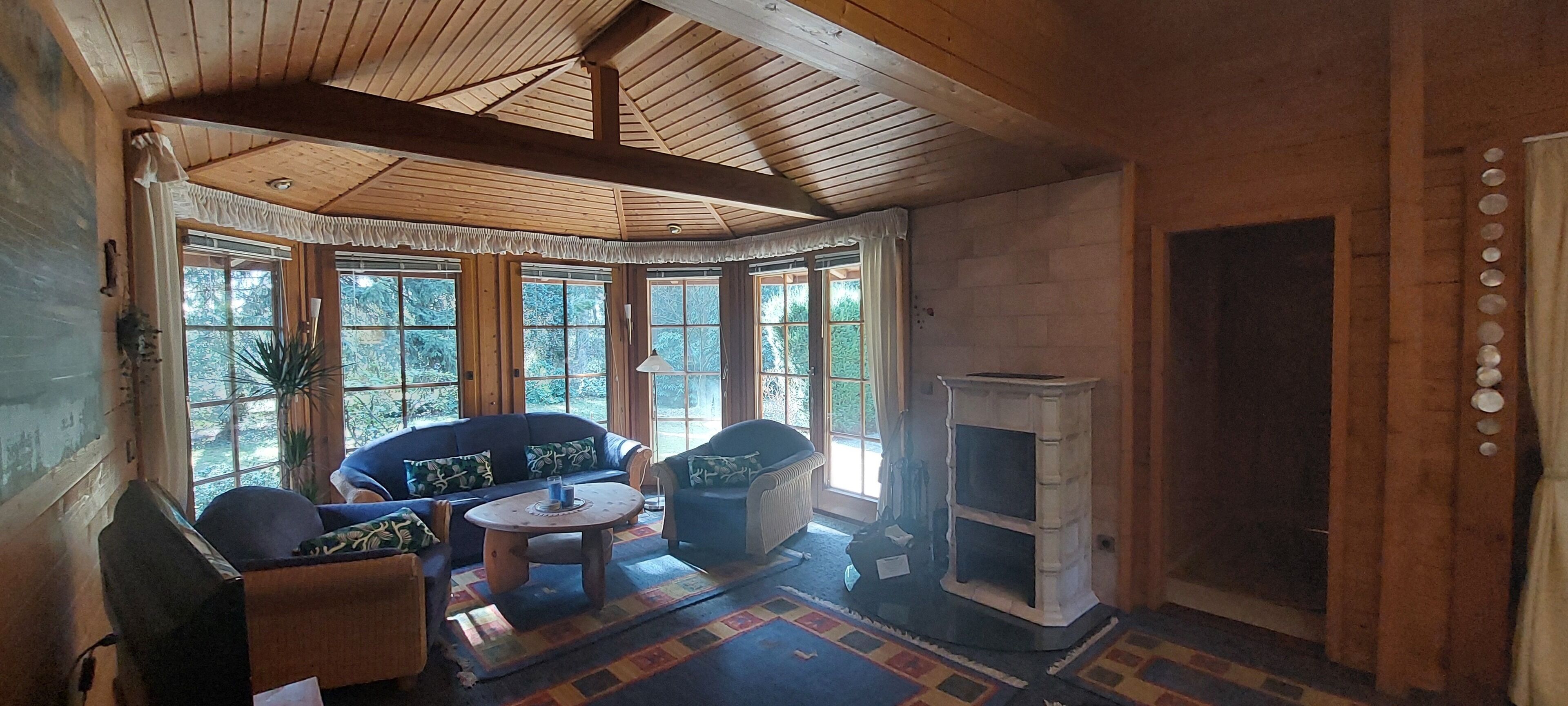 A cozy room with a wooden ceiling, large windows, a fireplace, and a sofa set.