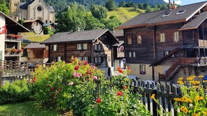 A traditional wooden building with a balcony, surrounded by a garden with flowers. - Vacation apartment with restaurant on the Aletsch Glacier in the Valais Alps<br> (Grengiols)