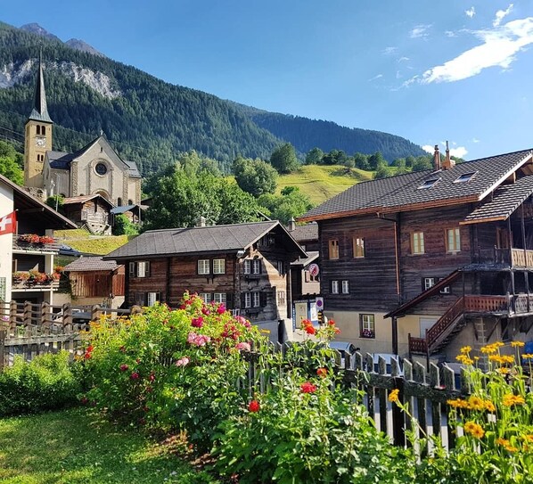 A traditional wooden building with a balcony, surrounded by a garden with flowers.