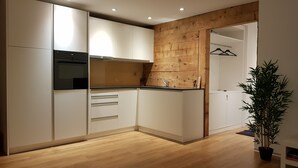 A modern kitchen with white cabinets, a wooden accent wall, and a black countertop. - Vacation apartment with restaurant on the Aletsch Glacier in the Valais Alps<br> (Grengiols)