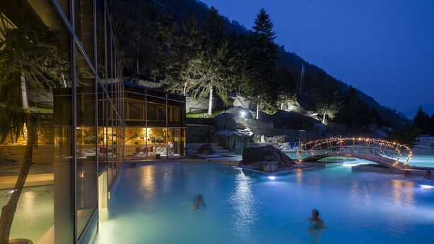 A pool area with a glass enclosure, a bridge, and a mountain backdrop. - Vacation apartment with restaurant on the Aletsch Glacier in the Valais Alps<br> (Grengiols)