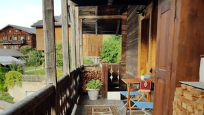 A wooden porch with a railing, a table, and a chair. There are two rugs on the floor. - Vacation apartment with restaurant on the Aletsch Glacier in the Valais Alps<br> (Grengiols)