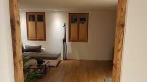A room with wooden flooring, a bed, a sofa, and two windows with shutters. - Vacation apartment with restaurant on the Aletsch Glacier in the Valais Alps<br> (Grengiols)
