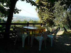 A round table with four white plastic chairs under a wooden fence, overlooking a scenic view of a city and countryside. - Nice small house with garden and breath-taking view over the Versilia Coast (Monteggiori)