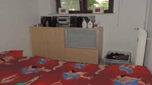 Ein Schlafzimmer mit einem Bett, einem Kleiderschrank, einem kleinen Schreibtisch mit einem Computer und einem Fenster.