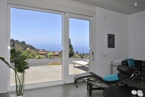 Ein Zimmer mit einer Schiebetür zum Balkon, einem Liegestuhl, einem kleinen Tisch und einem Topfpflanzen.