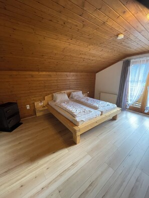 Un dormitorio con techo de madera, cama con ropa de cama blanca y un ventanal con cortinas.