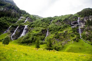 Un paisaje montañoso con múltiples cascadas y un prado con animales pastando.