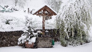 Un kiosque en bois, dont le toit est recouvert de neige, entouré d’arbres et d’arbustes chargés de neige.
