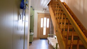 Un couloir avec un escalier en bois, une porte au fond et un porte-manteau sur la gauche.