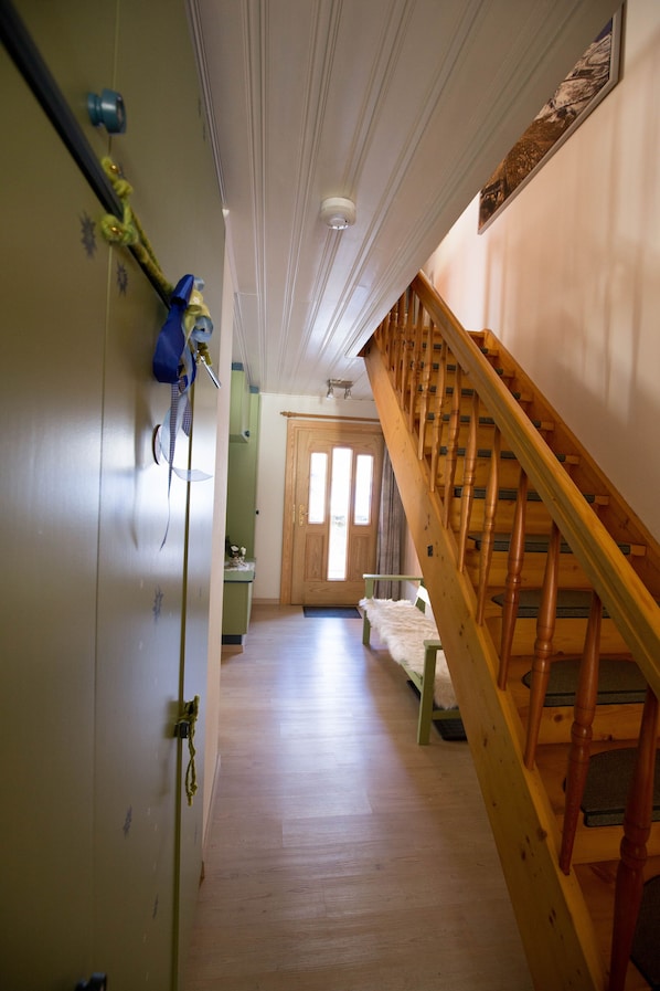 Un pasillo con una escalera de madera, una puerta al final y un perchero a la izquierda.