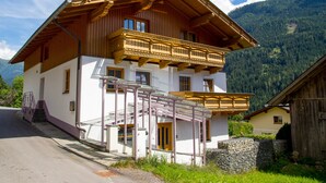 Une maison en bois à deux étages, dotée d’un balcon, d’un mur en pierre et surplombant un paysage montagneux.