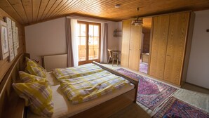 Une chambre avec un plafond en bois, un lit recouvert d’une courtepointe à carreaux, une fenêtre avec des rideaux, un radiateur et une armoire.