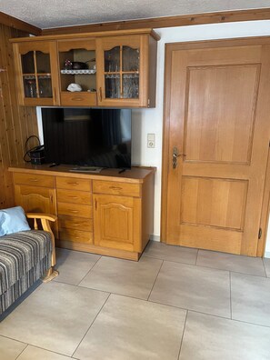 A room with a wooden cabinet, a television, a bed, and a door.