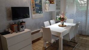 A modern dining area with a white table and chairs, a flat-screen TV mounted on the wall, and a decorative painting above the table. - Comfortable apartment, beach, pool, tennis, sailing, sea view, golf, diving (Le Pradet)