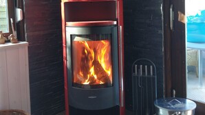 En vedeldad kamin med en glaslucka, en metallkastrull på sidan och en tegelvägg i bakgrunden.