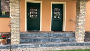 Een huis met twee groene deuren, een bakstenen gevel en een kleine veranda met treden naar de ingang.