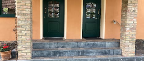 A house with two green doors, a brick exterior, and a small porch with steps leading to the entrance.
