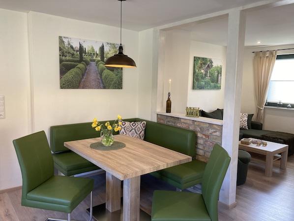 A dining area with a wooden table and green upholstered chairs, a pendant light, and a vase with yellow flowers. - Landlust Bergsdorf - pure relaxation! (Bergsdorf)