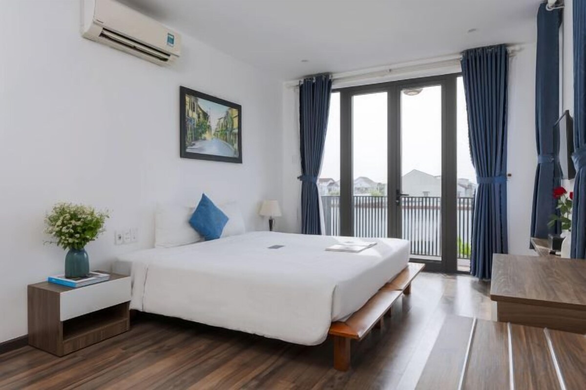 A hotel room with a bed, bedside table, and a view of the outdoors.