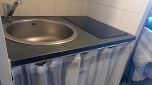 A kitchen with a stainless steel sink, a black countertop, and a curtain partially covering the sink area. - Furnished studio rental Winter/Summer Savoie ski area at the foot of the slopes (Villarembert)