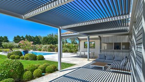 Zona d'estar exterior coberta amb piscina i jardí al fons.