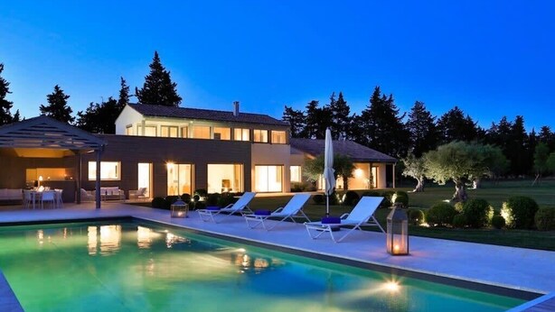 Una casa moderna amb piscina, gandules i una zona de terrassa ben il·luminada.