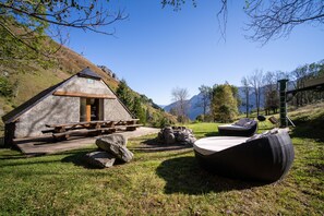 A rustic cabin with a wooden deck and a stone fireplace, surrounded by a grassy area and a view of mountains. - Spa, Sauna 10min from the ski slopes, Magnificent renovated sheepfold (Cauterets)
