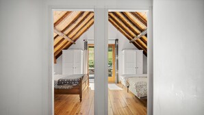 Ein Schlafzimmer mit Holzboden, zwei Betten und Blick ins Freie durch eine Tür.