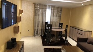 Een moderne woonkamer met een flatscreen televisie, een eethoek met een tafel en stoelen, een bank en een salontafel.