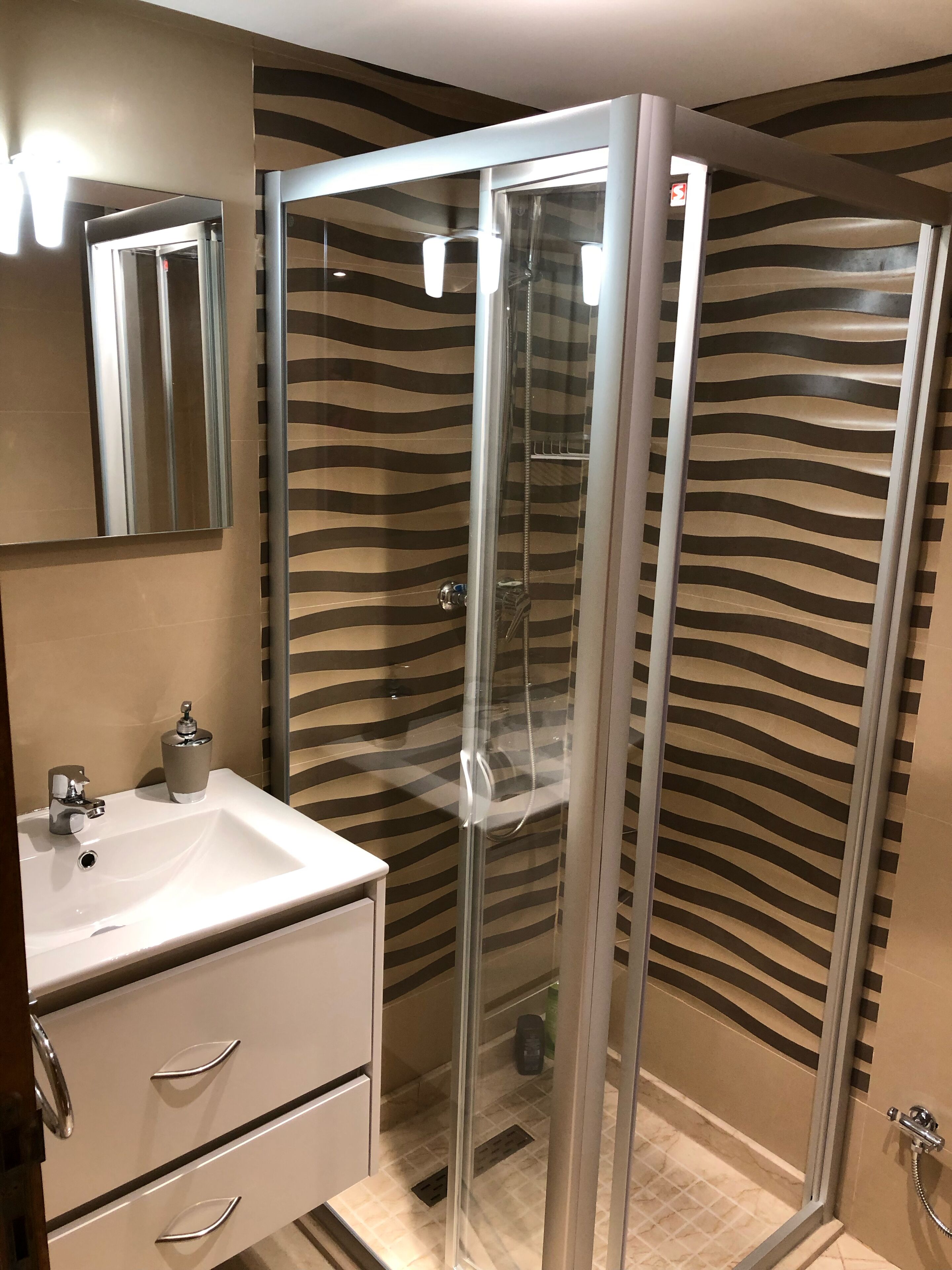 Een moderne badkamer met een douchecabine van glas, een witte wastafel en een spiegel.