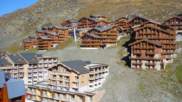 En grupp av träbyggda fjällstugor med balkonger, belägna vid en bergssluttning med steniga partier.