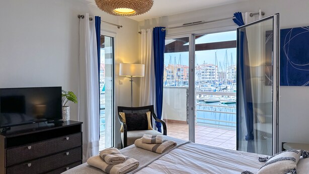 A hotel room with a bed, a TV, a desk, a chair, and a view of a marina.