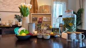A kitchen counter with various items including a bowl of fruits, a vase with flowers, a juicer, and a large water container.