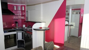 Cocina moderna con armarios blancos, estufa negra y una pared de acento color rosa. Hay una pequeña mesa redonda con dos sillas.