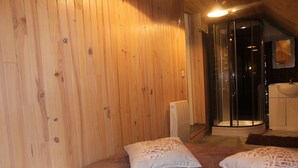 Habitación con paneles de madera, una cama, dos almohadas, cabina de ducha de vidrio y un lavamanos blanco.