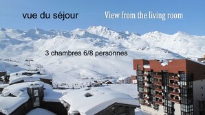 Vista nevada de una montaña desde una sala de estar con tres habitaciones visibles, cada una con capacidad para 6 u 8 personas.