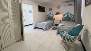 A bedroom with two beds, a nightstand, a chair, and a door leading to another room. - Breathtaking Beachfront Apartment - FREE Wi-Fi (Bridgetown)